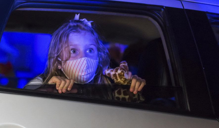 A child, wearing a protective face mask, watches a performance from inside a car, at the Hopi Hari horror theme amusement park, in the Vinhedo suburb of Sao Paulo, Brazil, Friday, Sept. 4, 2020. Due to the restrictions caused by COVID-19, the park created a drive-thru tour that allow the public to enjoy the experience by car. (AP Photo/Carla Carniel)