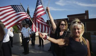 FILE - In this undated file photo, Melissa Moore, right, a Republican who is running for a seat in the Minnesota Legislature, waves an American flag with members of VFW 7051 in the background in St. Louis Park, Minn. Moore is among about two dozen legislative candidates in at least a dozen states who have shown varying levels of engagement with the QAnon conspiracy theory. “I like following it,” Moore said. “It’s an exciting movement that opens up our minds to different possibilities of what’s going on, of what’s really happening in our world today.” (Richard Tsong-Taatarii/Star Tribune via AP, File)