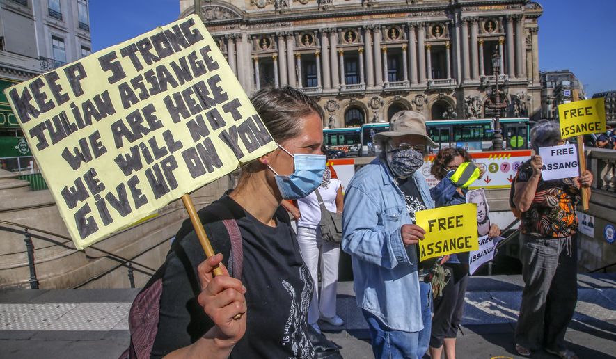 Demonstrators wearing protective face masks as precaution against the conoravirus stage a protest in Paris, Monday, Sept. 7, 2020. Lawyers for WikiLeaks founder Julian Assange and the U.S. government were squaring off in a London court on Monday at a high-stakes extradition case delayed by the coronavirus pandemic. Opera in the background. (AP Photo/Michel Euler)