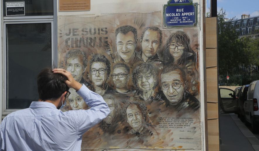 A man wearing a protective face mask as a precaution against the coronavirus looks on a painting by French street artist Christian Guemy, a.k.a. 'C215' in Paris Wednesday, Sept. 2, 2020, in tribute to the members of the satirical newspaper Charlie Hebdo attack by jihadist gunmen in January 2015. Thirteen men and a woman go on trial Wednesday over the 2015 attacks against a satirical newspaper and a kosher supermarket in Paris that marked the beginning of a wave of violence by the Islamic State group in Europe. Seventeen people and all three gunmen died during the three days of attacks in January 2015. (AP Photo/Michel Euler)
