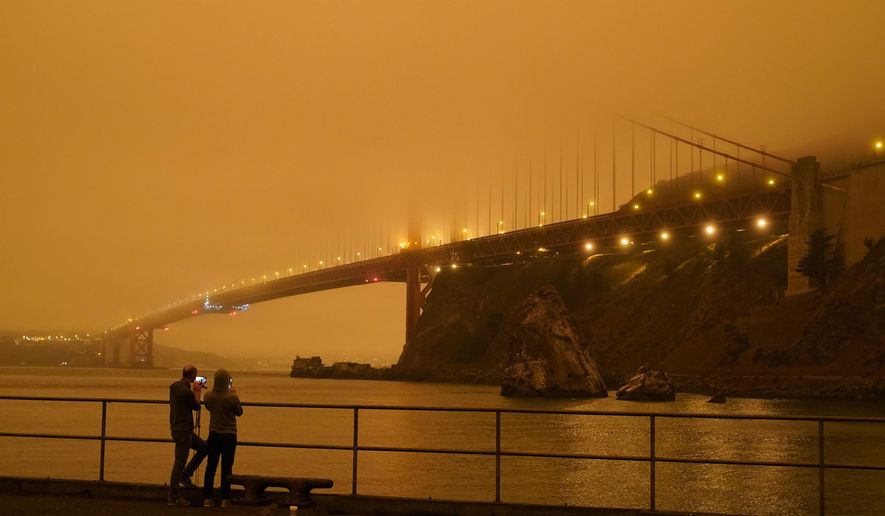 Patrick Kenefick, left, and Dana Williams, both of Mill Valley, Calif., record the darkened Golden Gate Bridge covered with smoke from wildfires Wednesday, Sept. 9, 2020, from a pier at Fort Baker near Sausalito, Calif. The photo was taken at 9:47 a.m. in the morning. (AP Photo/Eric Risberg)
