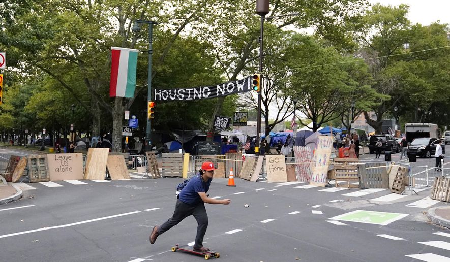 A man skateboards past a homeless encampment on the Benjamin Franklin Parkway, Wednesday, Sept. 9, 2020, in Philadelphia. City officials had ordered camp residents to leave by 9 a.m. Wednesday. (AP Photo/Matt Slocum)