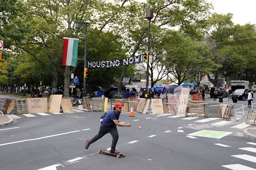 A man skateboards past a homeless encampment on the Benjamin Franklin Parkway, Wednesday, Sept. 9, 2020, in Philadelphia. City officials had ordered camp residents to leave by 9 a.m. Wednesday. (AP Photo/Matt Slocum)