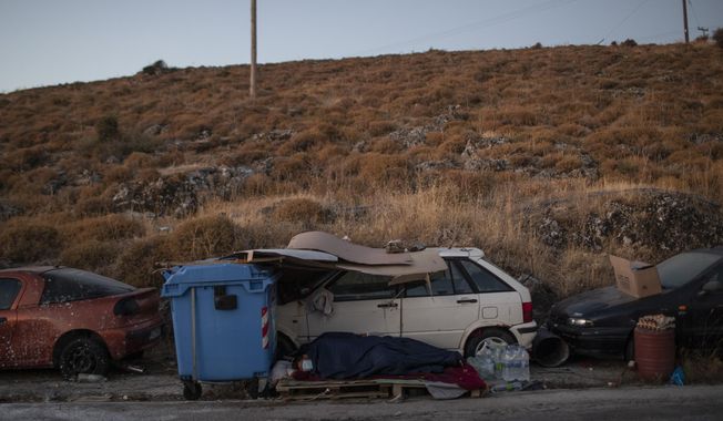 Migrants sleep on the roadside on the northeastern island of Lesbos, Greece, Friday, Sept. 11, 2020. The Greek government says thousands of migrants left homeless after fires gutted a sprawling refugee camp on the island of Lesbos will not be allowed to travel to mainland Greece. (AP Photo/Petros Giannakouris)
