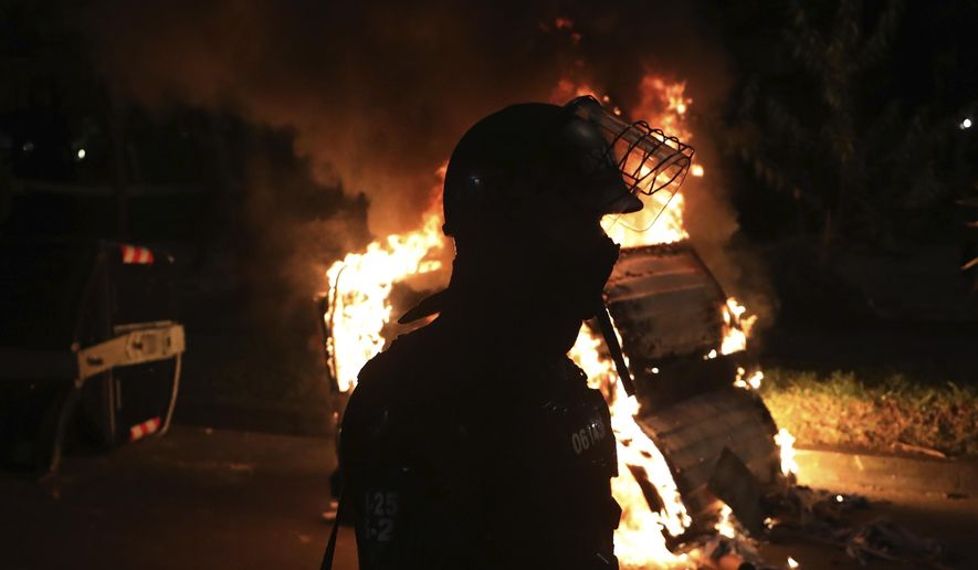 A police officer in riot gear stands behind a burning barricade during protests against the death of a man who was detained by police for violating social distancing rules to curb the spread of the new coronavirus, in Bogota, Colombia, Thursday, Sept. 10, 2020. Javier Ordonez died in a hospital Wednesday after receiving repeated electric shocks with a stun gun from officers who detained him, seen on a video taken by Ordonez&#39;s friend, and published on social media. (AP Photo/Fernando Vergara)