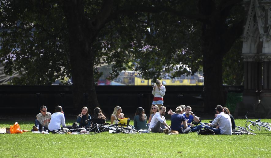 People sit on the grass at Victoria Gardens, in London, Thursday, Sept. 10, 2020. From Monday, social gatherings of more than six people will be banned in England — both indoors and outdoors — and Boris Johnson hinted that such restrictions will potentially remain in place until or through Christmas. (AP Photo/Alberto Pezzali)