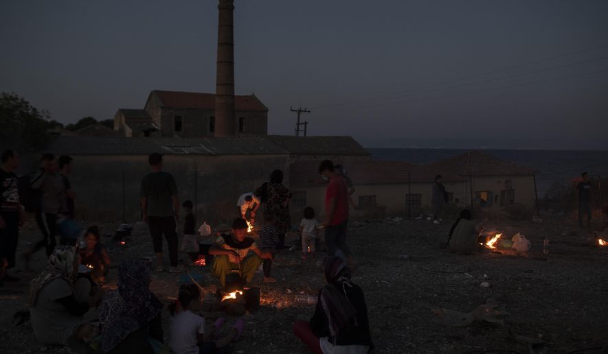 Refugees and migrants cook on makeshift fires near an abandoned factory in the island of Lesbos, Greece, Friday, Sept. 11, 2020.  Some thousands of refugees and migrants have spent a third night in the open on the Greek island of Lesbos after two consecutive nights of fires in the notoriously overcrowded Moria camp left them homeless. (AP Photo/Petros Giannakouris)