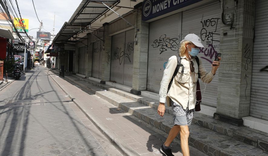 FILE - In this April 14, 2020, file photo, a foreign tourist walks along an empty road lined with closed shops in Bali, Indonesia. The Asian Development Bank has forecast Tuesday, Sept. 15, 2020 that developing economies in the region will contract in 2020, the first such downturn in nearly 60 years.  (AP Photo/Firdia Lisnawati, File)