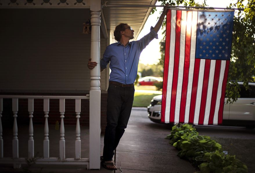 Outagamie County Executive Tom Nelson adjusts the American flag hanging off his front porch in Appleton, Wis., Aug. 18, 2020. (AP Photo/David Goldman/File)