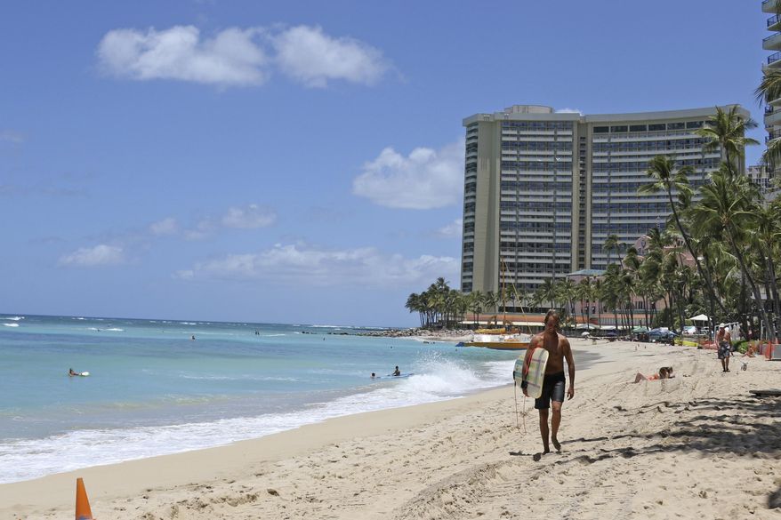 FILE - In this June 5, 2020, file photo, a surfer walks on a sparsely populated Waikiki Beach in Honolulu. Hawaii&#39;s governor says that starting Oct. 15, travelers arriving from out of state may bypass a 14-day quarantine requirement if they test negative for COVID-19. (AP Photo/Audrey McAvoy)