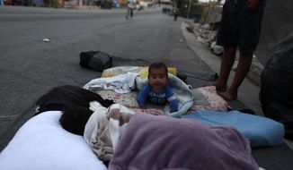 A baby crawls as migrants remained camped out on a road leading from Moria to the capital of Mytilene, on the northeastern island of Lesbos, Greece, Thursday, Sept. 17, 2020. Fires swept through the overcrowded camp at Moria on two nights last week, prompting more than 12,000 migrants and refugees to flee. Most of them remain without shelter even though emergency tents are available at another island site where a new camp is being built.  (AP Photo/Petros Giannakouris)