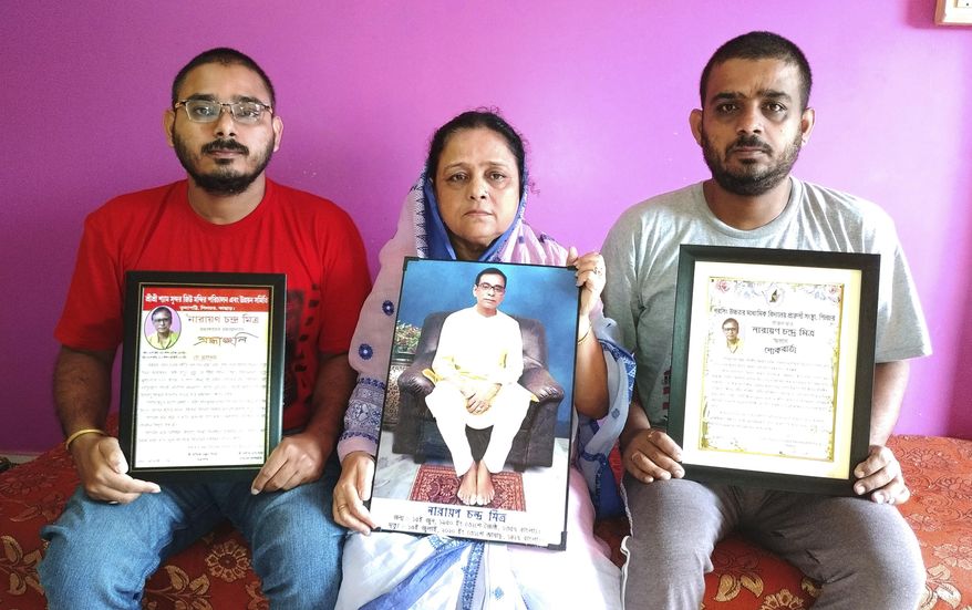 Anindita Mitra, 61, flanked by her sons Satyajit Mitra, right and Abhijit Mitra, pose with portraits of her husband late Narayan Mitra, at her house in Silchar, India, Sunday, Sept. 13, 2020. Narayan Mitra, wasn&#39;t listed among those killed by the coronavirus that authorities put out daily because the test results confirming COVID-19 arrived after his death. In India, people who die with other preexisting conditions are often not counted as COVID-19 deaths, while only those who test positive for the virus before dying are included in the official tally in many states. (AP Photo/Joy Roy)