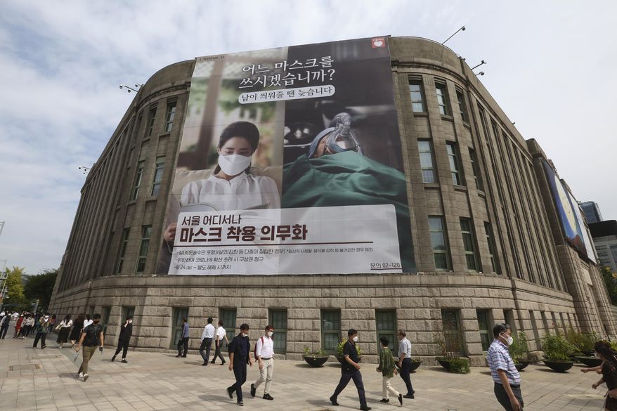 People wearing face masks to help protect against the spread of the coronavirus walk under a banner informing mandatory mask wearing in front of Seoul City Hall in Seoul, South Korea, Thursday, Sept. 17, 2020. The banner reads: " Which mask would you wear?" (AP Photo/Ahn Young-joon)