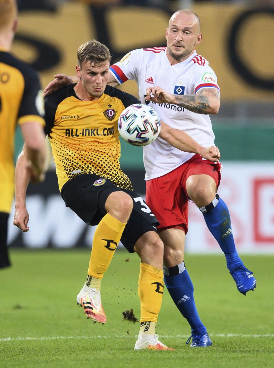 Hamburg's Toni Leistner, right, and Dresden's Christoph Daferner, left, challenge for the ball during the German soccer cup (DFB Pokal) first round match between SG Dynamo Dresden and Hamburger SV in Dresden, Germany, Monday, Sept. 14, 2020. Hamburg defender Toni Leistner has been banned for three games for assaulting a fan who he said had insulted his family. Leistner leapt into the stand during a TV interview and pushed a Dynamo Dresden fan after Dresden had beaten Hamburg 4-1 in their German Cup game Monday. (Robert Michael/dpa via AP)