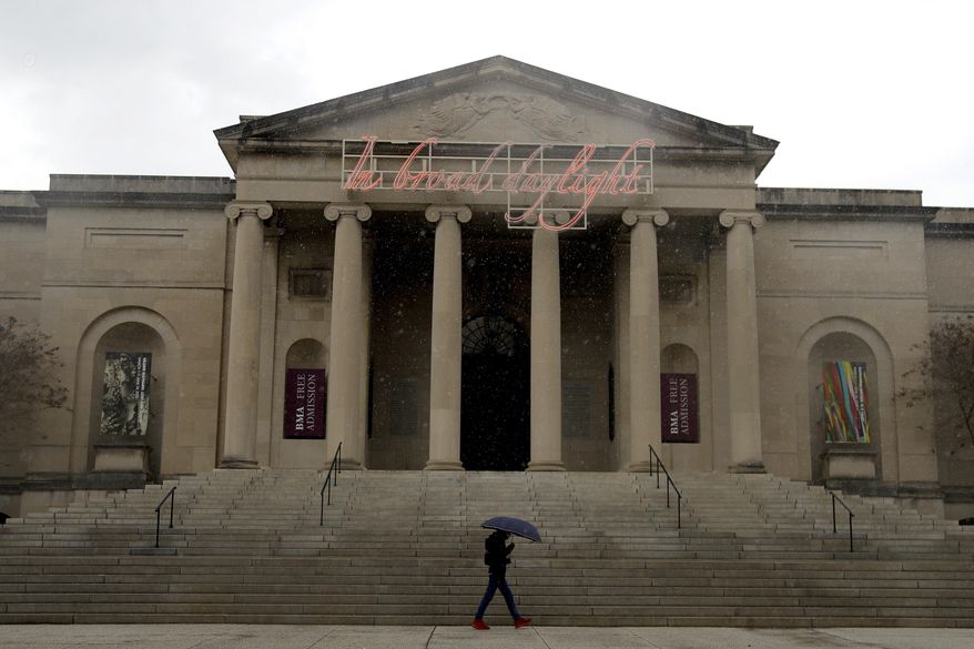 FILE - In this April 21, 2020 file photo, a man covers himself from rain with an umbrella as he walks in front of the Baltimore Museum of Art in Baltimore. With every face mask, bottle of hand sanitizer and pair of disposable gloves it acquires, the Baltimore Museum of Art is moving one more socially distanced step closer to reopening fully to the public, six months after locking its doors as the coronavirus pandemic descended on Maryland. The state’s largest museum began welcoming visitors Sept. 16, though the capacity was limited and galleries will reopen in phases. (AP Photo/Julio Cortez, File)