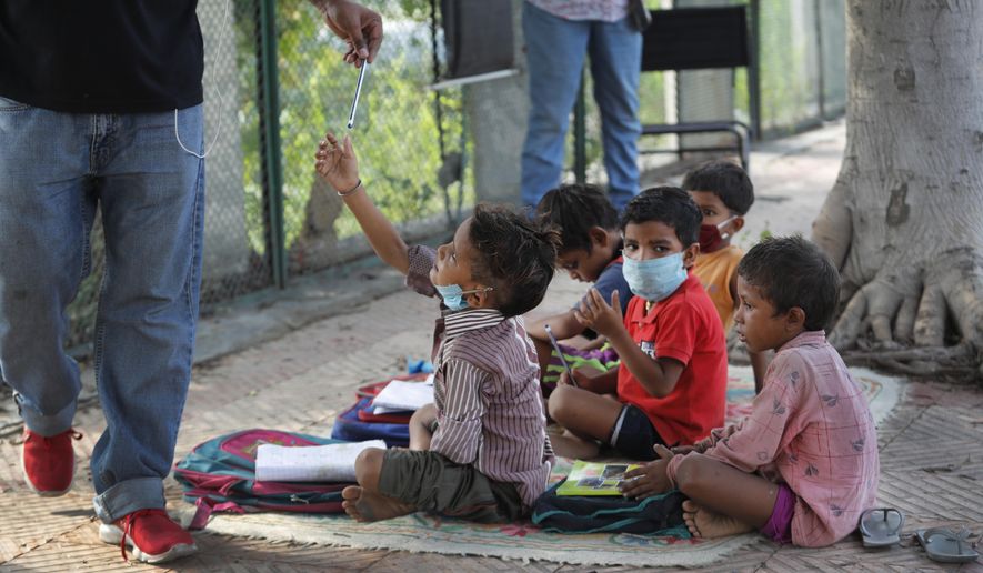 A child takes a pencil during a class conducted by Veena Gupta on a sidewalk in New Delhi, India, Thursday, Sept. 3, 2020. Veena Gupta and her husband are conducting free classes for underprivileged children on a sidewalk in New Delhi. As most schools in India remain shut since late March when the country imposed a nationwide lockdown to curb the spread of COVID-19, many switched to digital learning and taking classes online. (AP Photo/Manish Swarup)