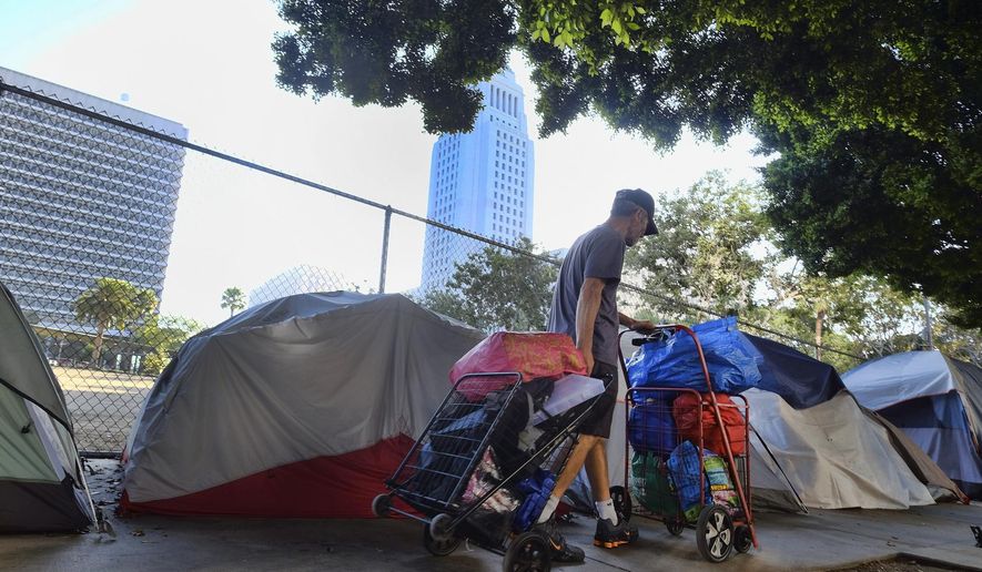 FILE - In this Monday, July 1, 2019, file photo, a homeless man moves his belongings from a street behind Los Angeles City Hall as crews prepared to clean the area. Over three days and nights this week, census takers are going to shelters, soup kitchens, mobile food van stops and other places across the U.S. where homeless people often gather. They will follow that with visits to encampments, under bridges, transit stations and other places where people live outside. (AP Photo/Richard Vogel, File)