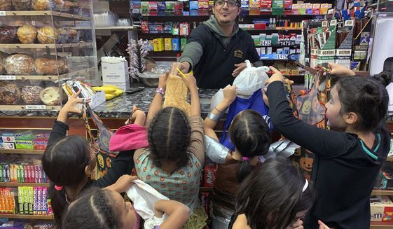 In this Oct. 31, 2018 file photo, a local convenience store worker, hands out candy to trick or treaters on Halloween in Brooklyn Borough of New York. Montgomery County, Md., on Oct. 2 cautioned its residents to not take their kids trick or treating this Halloween out of concern to keep down transmission of the novel coronavirus. (AP Photo/Wong Maye-E)  **FILE**