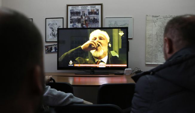 In this Wednesday, Nov. 29, 2017 file photo, Bosnian people watch the live TV broadcast from the International Criminal Court for the former Yugoslavia (ICTY) in The Hague as Slobodan Praljak brings a bottle to his lips, in southern Bosnian town of Mostar 140 kms south of Sarajevo. Julian Assange relayed how he “binge-watched” the suicide of the former Bosnian Croat general in a United Nations courtroom three years ago, a doctor who visited the WikiLeaks founder on several occasions while he was in the Ecuadorian Embassy in London told an extradition hearing Thursday, Sept, 24, 2020.  (AP Photo/Amel Emric, file)