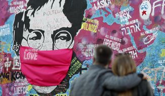 FILE - A couple look at the &amp;quot;Lennon Wall&amp;quot; with a face mask attached to the image of John Lennon, in Prague, Czech Republic, on April 6, 2020. Like so many other events in the year of coronavirus, an annual tribute to John Lennon held in its adopted city of New York will go online. The five-hour event will be streamed for free on Lennon&#39;s birthday, October 9, starting at 7 p.m. Eastern time on the LennonTribute.org website. It will feature recorded performances from Patti Smith, Rosanne Cash, Natalie Merchant, Jackson Browne, Jorma Kaukonen and others. (AP Photo/Petr David Josek)