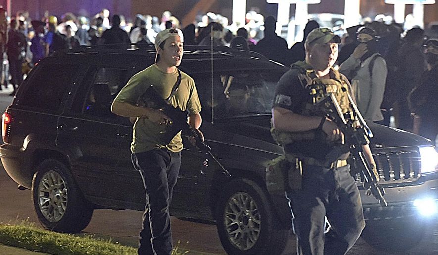 FILE - In this Aug. 25, 2020, file photo, Kyle Rittenhouse, left, with backwards cap, walks along Sheridan Road in Kenosha, Wis., with another armed civilian. Attorney John Price who is representing Kyle Rittenhouse, charged with shooting three people during a protest in Kenosha, Wisconsin, has resigned from his position with a defense fund that has raked in more than $700,000 to defend his client and conservative causes. (Adam Rogan/The Journal Times via AP, File)