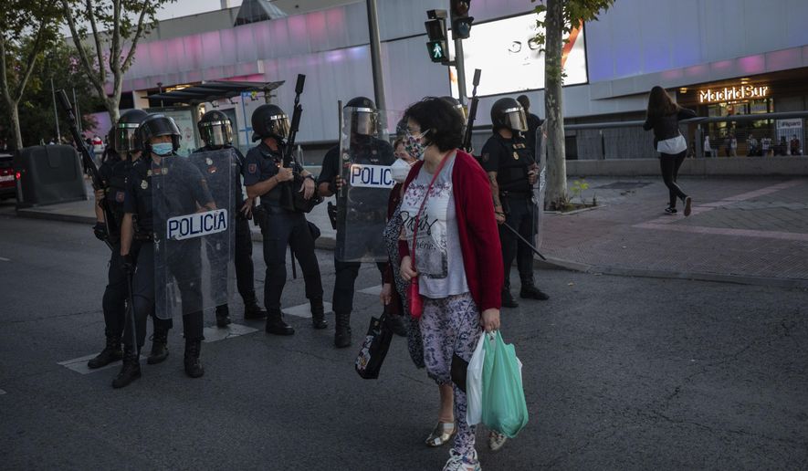 Two neighbours of restricted mobility areas in Madrid due to the coronavirus outbreak cross the street in front an anti-riot police unit short after a residents protest demanding more resources for public health system and against social inequality in the southern neighbourhood of Vallecas, Madrid, Spain, Thursday, Sept. 24, 2020. The regional government is set to announce Friday new restrictions in Madrid, where gatherings are limited to a maximum of 6 people and more than 850,000 residents have been partially locked down this week. (AP Photo/Bernat Armangue)