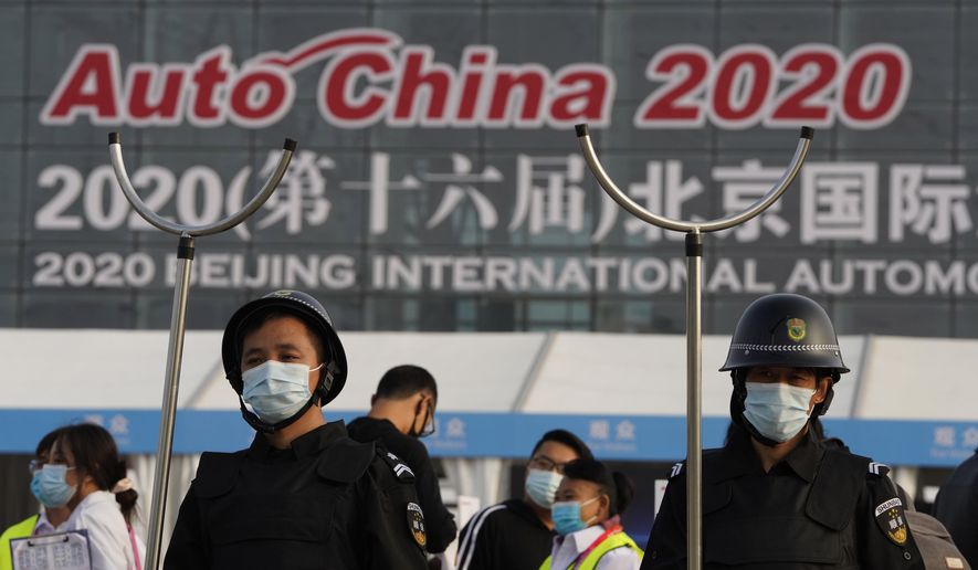 Security guards wearing masks and armed with restrainers stand guard at the entrance to the Auto China 2020 show in Beijing, China on Saturday, Sept. 26, 2020. The auto show, the first major in-person sales event for any industry since the coronavirus pandemic began, opens Saturday in a sign the ruling Communist Party is confident China has contained the disease. Still, automakers face intensive anti-virus controls including quarantines for visitors from abroad and curbs on crowd sizes at an event that usually is packed shoulder-to-shoulder with spectators. (AP Photo/Ng Han Guan)