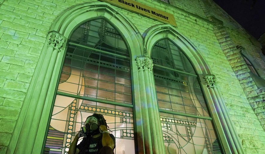 A protester wears a gas mask outside The First Unitarian church, Thursday, Sept. 24, 2020, in Louisville, Ky. Authorities pleaded for calm while activists vowed to fight on Thursday in Kentucky's largest city, where a gunman wounded two police officers during anguished protests following the decision not to charge officers for killing Breonna Taylor. (AP Photo/John Minchillo)