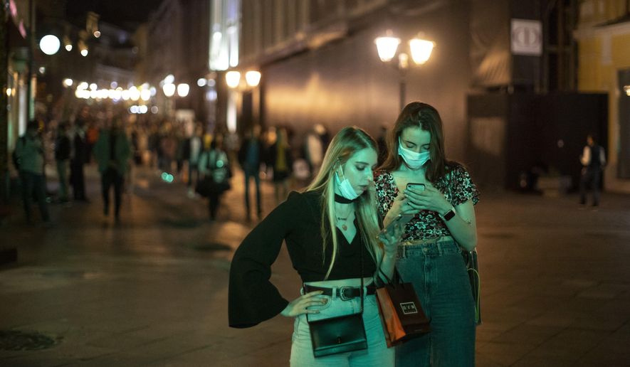 Two women wearing face masks to protect against coronavirus look at a smartphone in the center of Moscow, Russia, Friday, Sept. 25, 2020. Moscow authorities have issued a recommendation for the elderly to stay at home and for employers to allow as many people as possible to work remotely, following a rapid growth of the coronavirus caseload in the Russian capital. (AP Photo/Alexander Zemlianichenko)