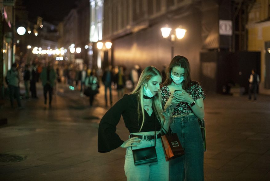 Two women wearing face masks to protect against coronavirus look at a smartphone in the center of Moscow, Russia, Friday, Sept. 25, 2020. Moscow authorities have issued a recommendation for the elderly to stay at home and for employers to allow as many people as possible to work remotely, following a rapid growth of the coronavirus caseload in the Russian capital. (AP Photo/Alexander Zemlianichenko)