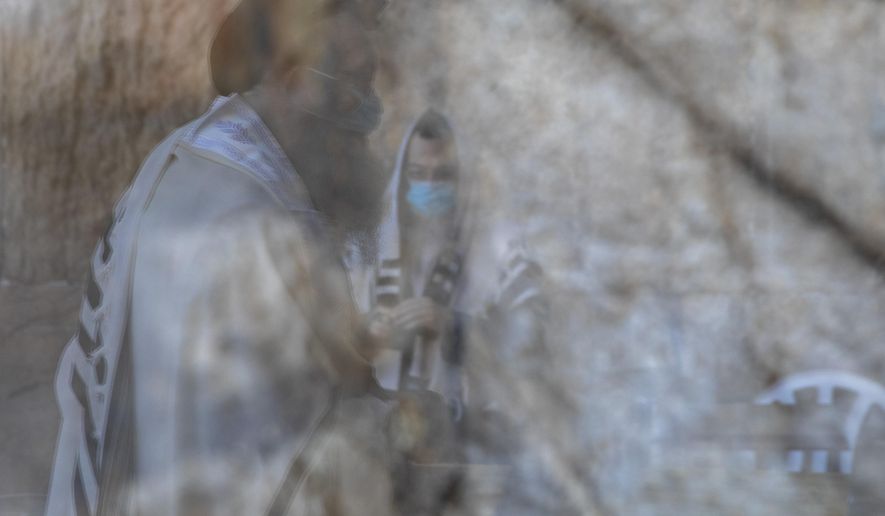 Ultra-Orthodox Jewish men wearing face masks, are reflected on a door window, as they pray ahead of Yom Kippur, the holiest day in the Jewish year which starts at sundown Sunday during a three-week nationwide lockdown to curb the spread of the coronavirus at the Western Wall, the holiest site where Jews can pray in Jerusalem's old city, Sunday, Sept. 27, 2020. (AP Photo/Ariel Schalit)