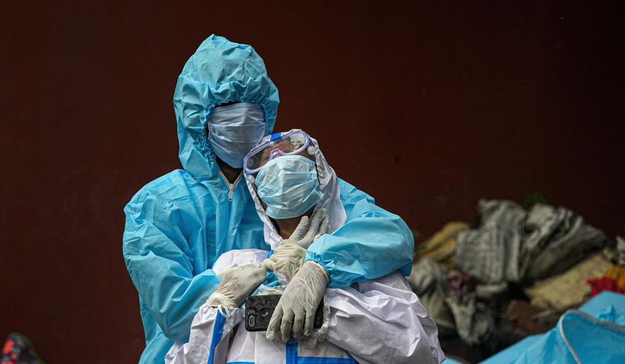 FILE - In this Sept. 10, 2020, file photo, a woman wearing white protective gear, foreground, mourns after taking a glimpse of her husband's body, a victim of COVID 19, at a cremation site in Gauhati, India. The worldwide death toll from the coronavirus eclipsed 1 million, nine months into a crisis that has devastated the global economy, tested world leaders' resolve, pitted science against politics and forced multitudes to change the way they live, learn and work. (AP Photo/Anupam Nath, File)