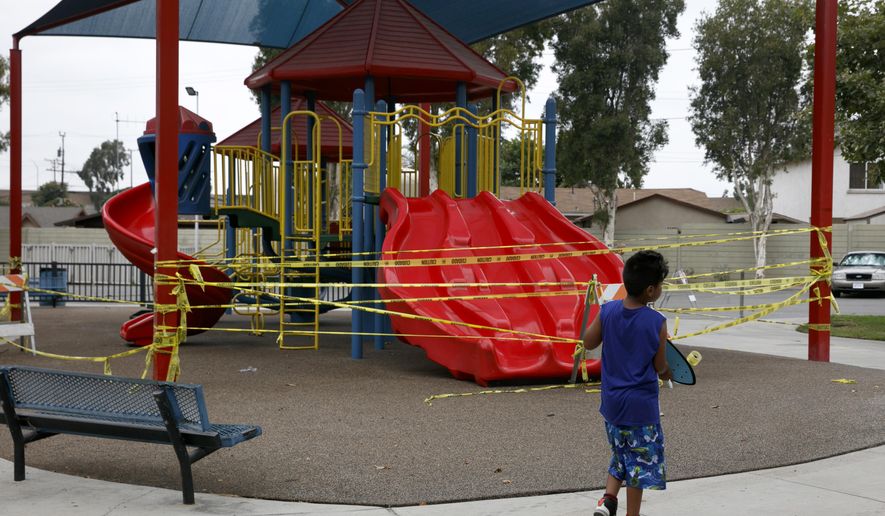 FILE - In this July 1, 2020 file photo, a boy walks with his skateboard past a playground sealed off due to the coronavirus pandemic in Commerce, Calif. California public health officials say it's OK for public playgrounds to open across the state. The new guidelines require face coverings for everyone 2 and older and physical distancing between people who don't live in the same household. On Tuesday, Sept. 29, 2020, state public health officials officially loosened restrictions in 11 counties, allowing more businesses to reopen. (AP Photo/Jae C. Hong, File)