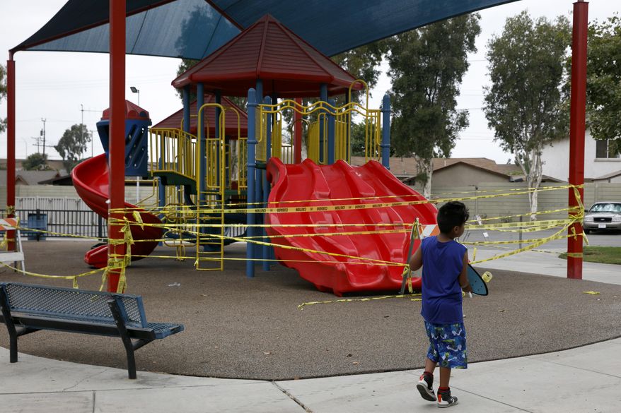 FILE - In this July 1, 2020 file photo, a boy walks with his skateboard past a playground sealed off due to the coronavirus pandemic in Commerce, Calif. California public health officials say it's OK for public playgrounds to open across the state. The new guidelines require face coverings for everyone 2 and older and physical distancing between people who don't live in the same household. On Tuesday, Sept. 29, 2020, state public health officials officially loosened restrictions in 11 counties, allowing more businesses to reopen. (AP Photo/Jae C. Hong, File)