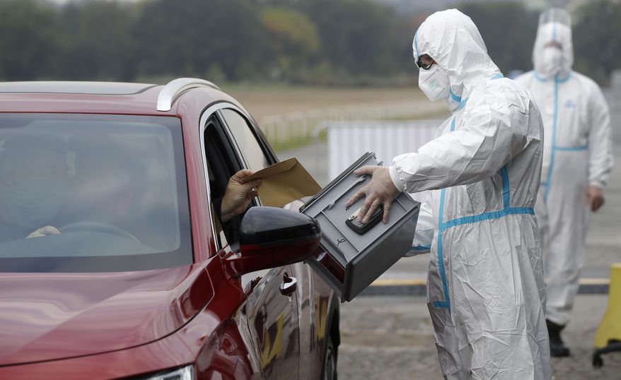 An election committee member, wearing a protective suit, holds a ballot box for a man to vote in regional and senate elections at a drive-in polling station in Prague, Czech Republic, Wednesday, Sept. 30, 2020. Czechs are casting ballots from their cars for the first time, a measure forced by the coronavirus pandemic. A total of 156 drive-in temporary ballot stations have been established by the armed forces across the country for those quarantined due to COVID-19. (AP Photo/Petr David Josek)