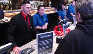 Customers make bets at the William Hill sportsbook inside the Tropicana casino in Atlantic City N.J., on March 8, 2019. Caesars Entertainment announced Wednesday, Sept. 30, 2020, it is buying William Hill for $3.7 billion. (AP Photo/Wayne Parry)