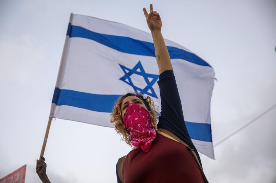 Israeli protesters wave flags and chant slogans during a demonstration against parliament's plans to ban them from protesting during the current nationwide lockdown due to the coronavirus pandemic, in Tel Aviv, Israel, Tuesday, Sept. 29, 2020. The protesters accuse Prime Minister Benjamin Netanyahu of exploiting the coronavirus crisis in order to stop weeks of demonstrations against him. (AP Photo/Oded Balilty)