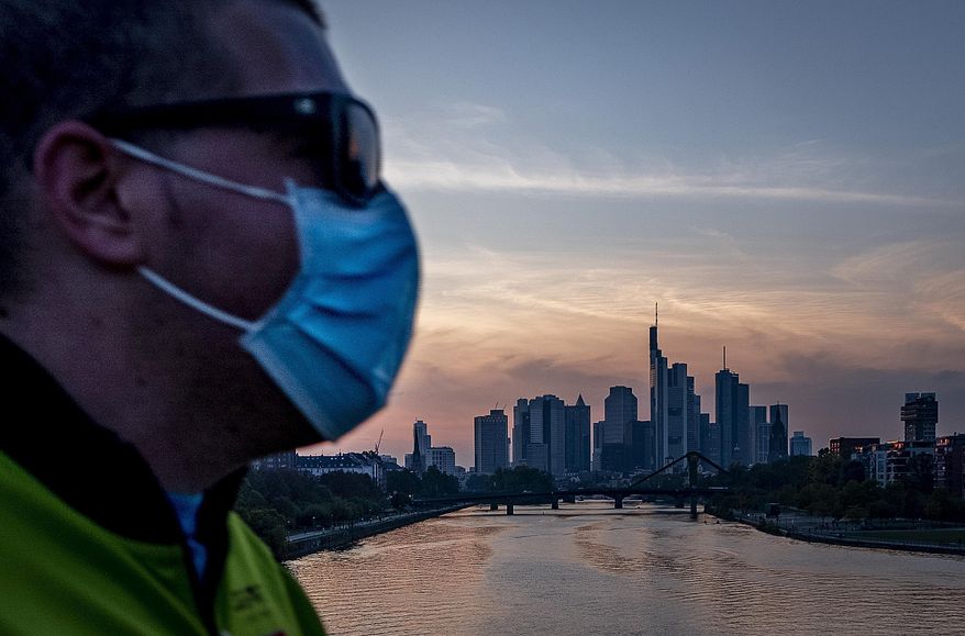 A man wears a face mask as he walks across the bridge over the river Main in Frankfurt, Germany, Wednesday, Sept. 30, 2020. (AP Photo/Michael Probst)