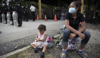 An Honduran migrant and her daughter sit at a roadblock set by security forces in Poptun, Guatemala, Friday, Oct. 2, 2020. Guatemala vowed to detain and return members of a new caravan of hundreds of migrants that set out from neighboring Honduras in hopes of reaching the United States, saying they represent a health threat amid the coronavirus pandemic. (AP Photo/Moises Castillo)