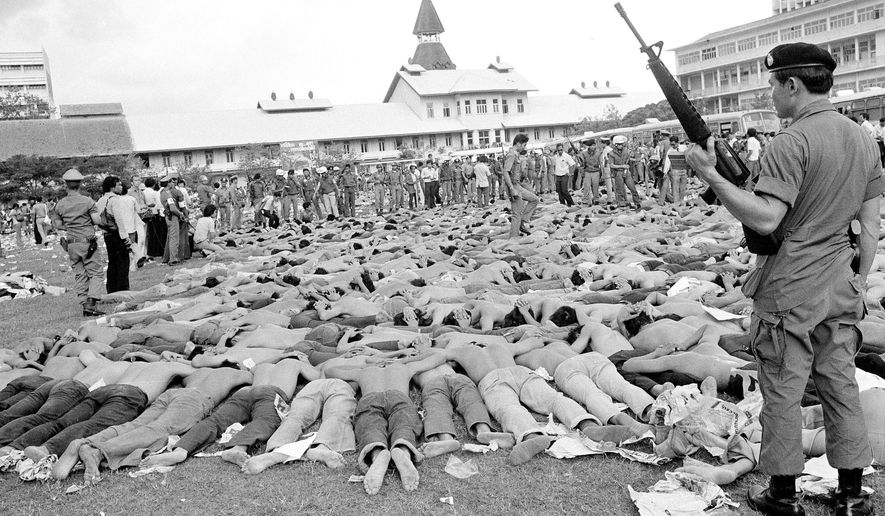 FILE - In this Oct. 6, 1976, file photo, police stand guard over leftist Thai students on a soccer field at Thammasat University, in Bangkok, Thailand. This year’s anti-government protests are seeking new elections, a more democratic constitution and an end to intimidation of political activists. Their speeches have repeatedly highlighted the 1976 tragedy, piquing the interest of the current generation in what their forebears faced. (AP Photo/Gary Mangkorn, File)