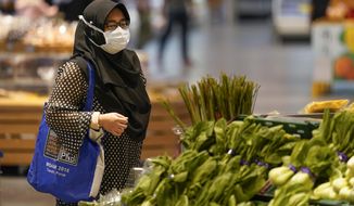 A shopper wearing a face mask to help curb the spread of the coronavirus looks at produce and a grocery in Putrajaya, Malaysia, Monday, Oct. 5, 2020. Prime Minister Muhyiddin Yassin says he will self-quarantine after a Cabinet minister he was in contact with tested positive for the coronavirus. (AP Photo/Vincent Thian)