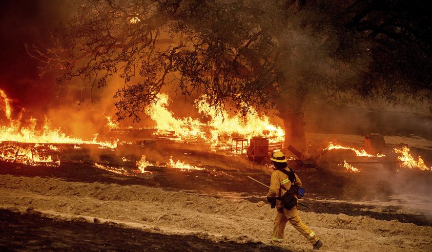 In this Oct. 1, 2020 file photo a firefighter passes flames while battling the Glass Fire in a Calistoga, Calif., vineyard. With months still to go in California&#39;s fire season, the state has already shattered records for the amount of land scorched in a single year, more than 4 million acres to date, with one blaze alone surpassing the 1 million-acre mark. Five of the 10 largest wildfires in state history have occurred since August. (AP Photo/Noah Berger, File)  **FILE**