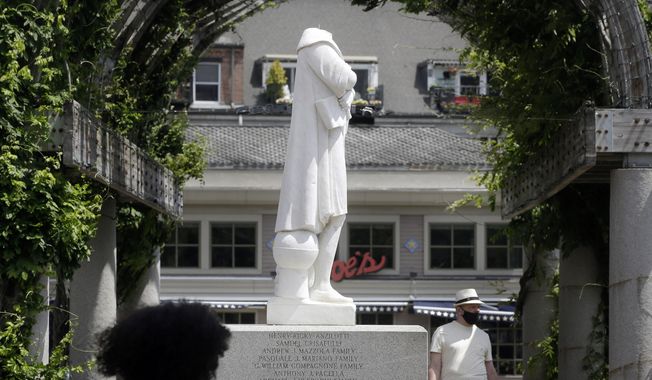 FILE - in this June 10, 2020, file photo, people walk near a damaged Christopher Columbus statue in a waterfront park near the Boston&#x27;s traditionally Italian North End neighborhood. The statue, removed after it was beheaded, won&#x27;t be returned to its original location. Instead the repaired statue will be placed at the North End chapter of the Knights of Columbus where it will be publicly displayed. (AP Photo/Steven Senne, File)