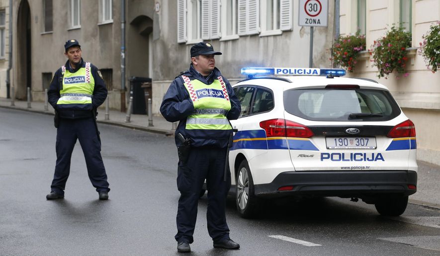 Police officers stand watch next to a police car on a street in Zagreb, Croatia, Monday Oct. 12, 2020 in the vicinity of a shooting incident. A gunman on Monday shot and wounded a police officer outside the Croatian government headquarters in the capital, Zagreb, before killing himself, police said. The shooting happened around 8 a.m. at Trg Svetog Marka, or St. Mark's Square, which hosts the Croatian parliament building and other other important state institutions. (AP Photo/Darko Bandic)