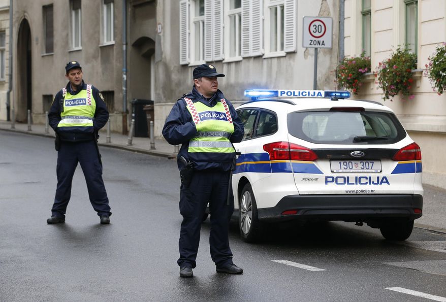 Police officers stand watch next to a police car on a street in Zagreb, Croatia, Monday Oct. 12, 2020 in the vicinity of a shooting incident. A gunman on Monday shot and wounded a police officer outside the Croatian government headquarters in the capital, Zagreb, before killing himself, police said. The shooting happened around 8 a.m. at Trg Svetog Marka, or St. Mark's Square, which hosts the Croatian parliament building and other other important state institutions. (AP Photo/Darko Bandic)