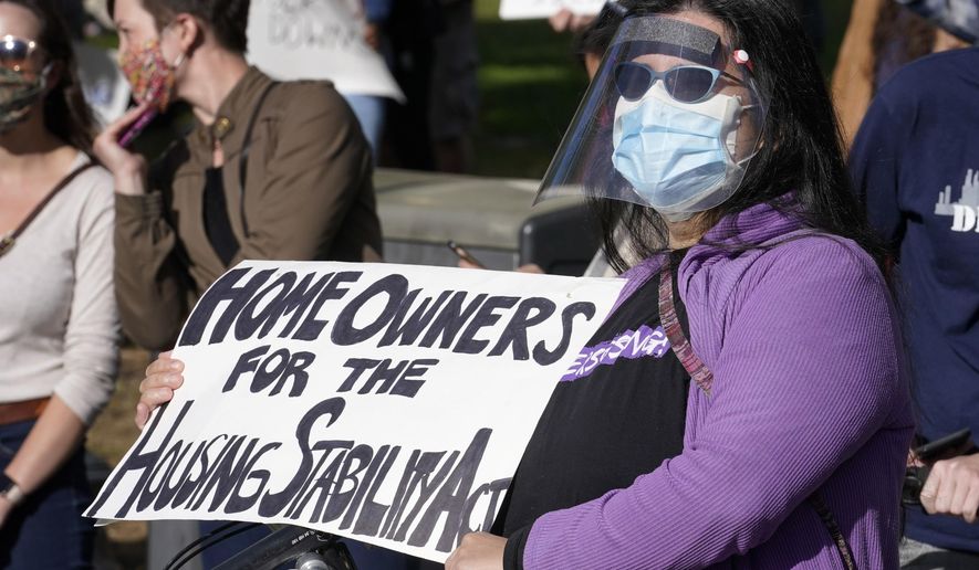 Maria Blanco, of Boston, right, displays a placard during a demonstration held to show support for tenants and homeowners at risk of eviction, Sunday, Oct. 11, 2020, on the Boston Common, in Boston, as the state weathers the ongoing COVID-19 crisis. The event was part of a series of actions across the commonwealth in support of the Guaranteed Housing Stability bill leading up to the expiration Massachusetts' eviction and foreclosure moratorium, which is set to end on Oct. 17. (AP Photo/Steven Senne)