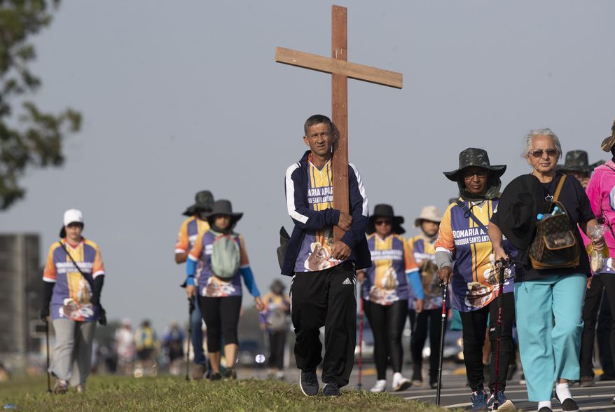 Pilgrims walk on the shoulder of a highway toward Our Lady of Aparecida Basilica on the outskirts of Aparecida, Brazil, Monday, Oct. 12, 2020. Two of Brazil’s biggest Catholic celebrations scheduled for this holiday weekend were downscaled and canceled, yet people still appeared in droves, underscoring the challenge of extolling COVID-19 precautions as well as pressures to ease up. (AP Photo/Andre Penner)