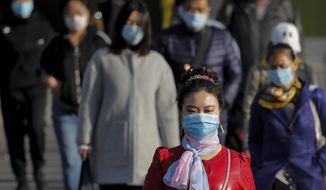 People wearing face masks to help curb the spread of the coronavirus walk across a street during the morning rush hour in Beijing, Tuesday, Oct. 13, 2020. (AP Photo/Andy Wong)