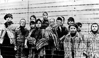 A picture taken just after the liberation by the Soviet army in January 1945, shows a group of children wearing concentration camp uniforms at the time behind barbed wire fencing in the Oswiecim (Auschwitz) Nazi concentration camp. Germany has agreed to provide more than a half-billion euros to aid Holocaust survivors struggling under the burdens of the coronavirus pandemic, the organization that negotiates compensation with the German government said Wednesday. (AP Photo/CAF pap, file)