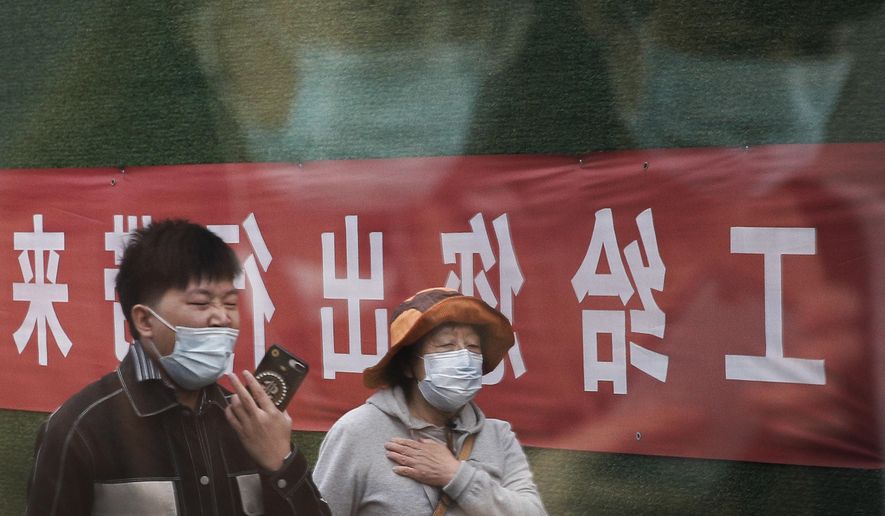 Commuters wearing face masks to help curb the spread of the coronavirus are reflected on a window panel as others walk by an office building under renovation in Beijing, Wednesday, Oct. 14, 2020. (AP Photo/Andy Wong)